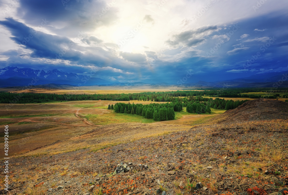The high-mountainous steppe Chuiskaya in the rays of the sun because of the clouds of a group of trees stony land and on the mountain zone there are high mountains with Aktru glaciers in Gorny Altai The high-mountainous steppe Chuiskaya in the rays of the sun because of the clouds of a group of trees stony land and on the mountain zone there are high mountains with Aktru glaciers in Gorny Altai