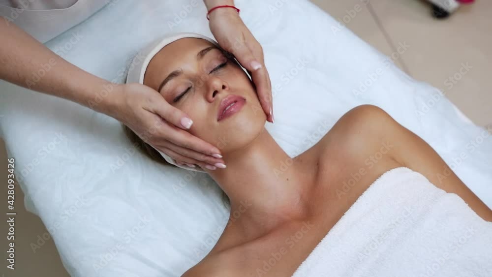 Face massage at spa salon. Doctor hands. Pretty female patient. Beauty treatment. Healthy skin procedure. Young woman head. Light background. Scrub rejuvenation. Facial dermatology mask. Detox therapy Face massage at spa salon. Doctor hands. Pretty female patient. Beauty treatment. Healthy skin procedure. Young woman head. Light background. Scrub rejuvenation. Facial dermatology mask. Detox therapy