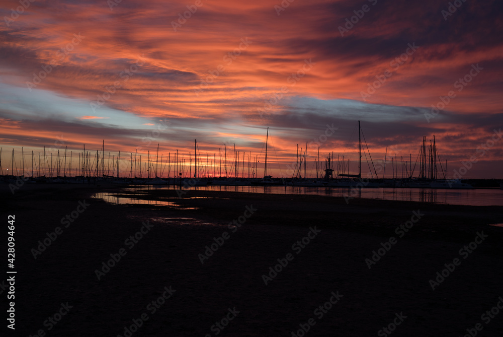 Silhouetted sailboats on orange color seascape over sunset sky.	