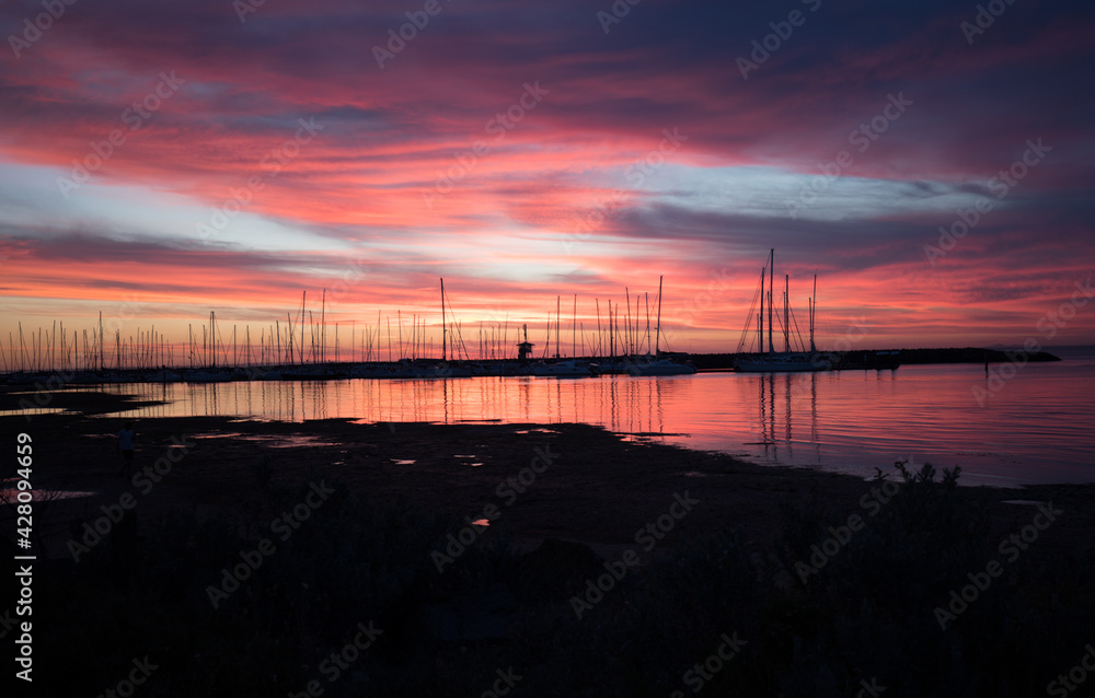 Silhouetted sailboats on orange color seascape over sunset sky.	