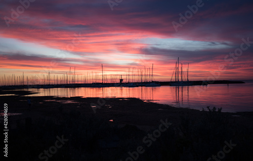 Silhouetted sailboats on orange color seascape over sunset sky. 