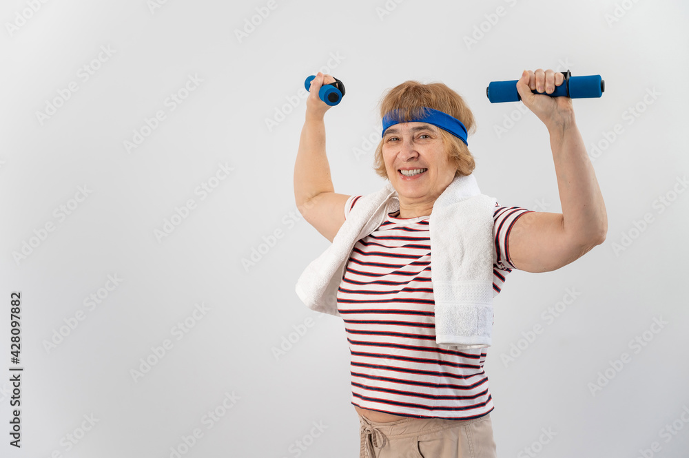 An elderly woman with a blue bandage on her head trains with dumbbells on a white background An elderly woman with a blue bandage on her head trains with dumbbells on a white background