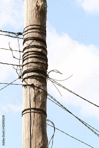 electrical wires coiled on a wooden pole against a blue sky and white clouds, Old-style phone poles and cables. Cables in the air. Clear sky.