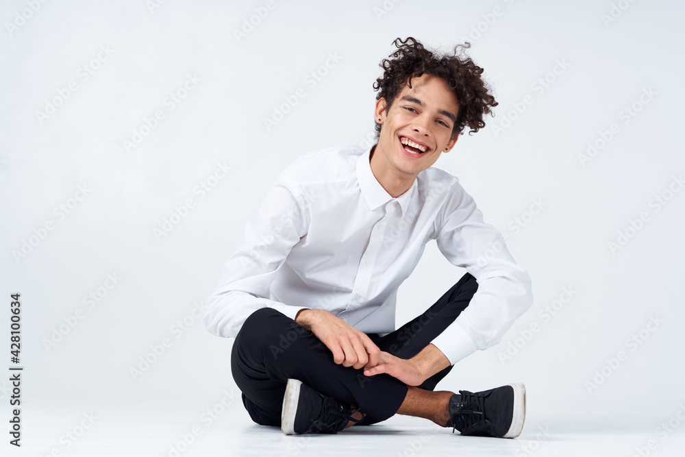 a guy in trousers in sneakers and a shirt sits on the floor and gestures with his hands a guy in trousers in sneakers and a shirt sits on the floor and gestures with his hands