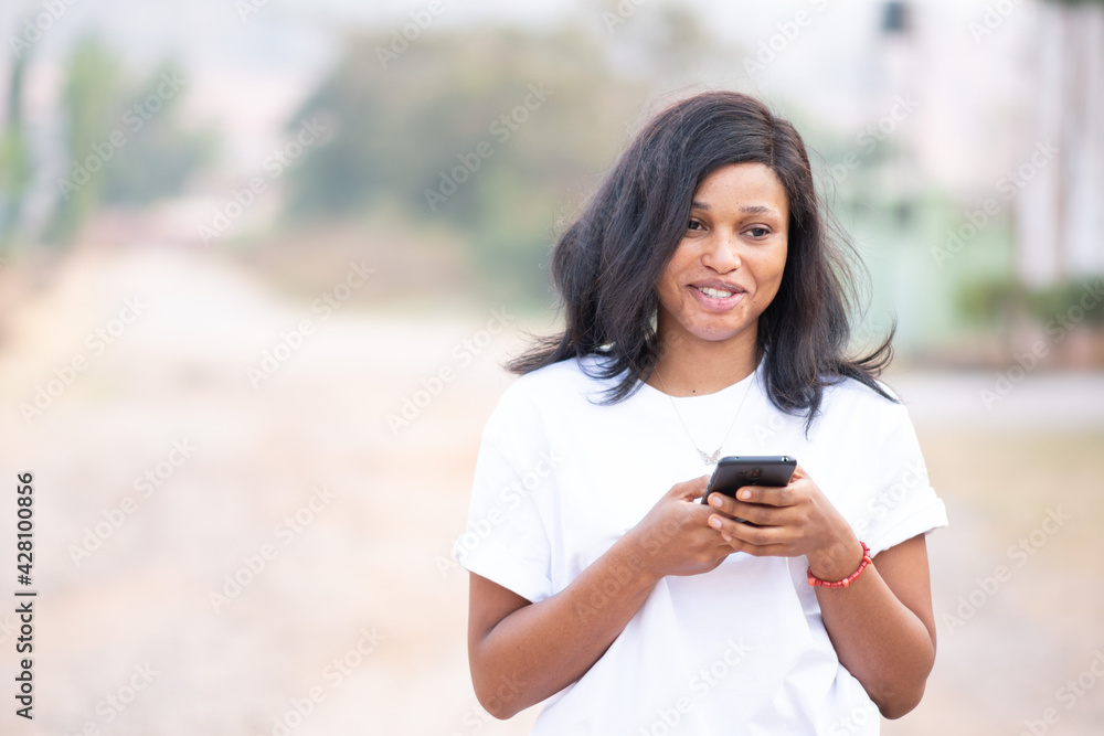 beautiful young black lady using her mobile phone to text on a bright day beautiful young black lady using her mobile phone to text on a bright day