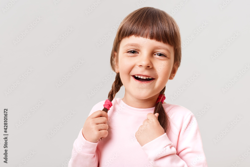 Little European cute laughing girl in casual jumper looking diretcly at camera, touching her pigtails, laughing happily isolated over white background, wearing casually. Little European cute laughing girl in casual jumper looking diretcly at camera, touching her pigtails, laughing happily isolated over white background, wearing casually.