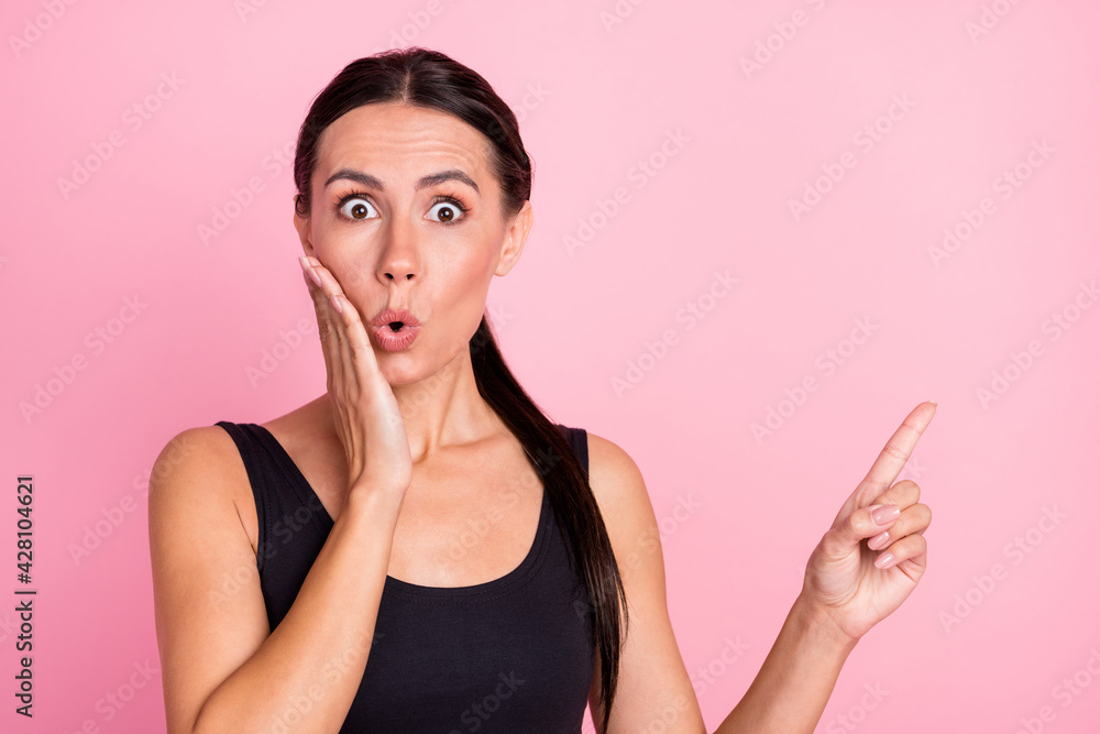 Obraz premium Photo of amazed shocked young woman point finger empty space hold hand cheek isolated on pink color background