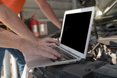 Car repairs. A car mechanic is using a laptop computer to check the engine operation.