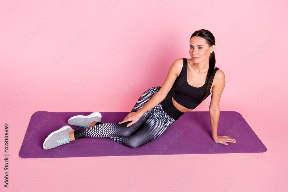 Full length photo of young sportive girl happy smile sit mat relax exercises look empty space isolated over pink color background Full length photo of young sportive girl happy smile sit mat relax exercises look empty space isolated over pink color background