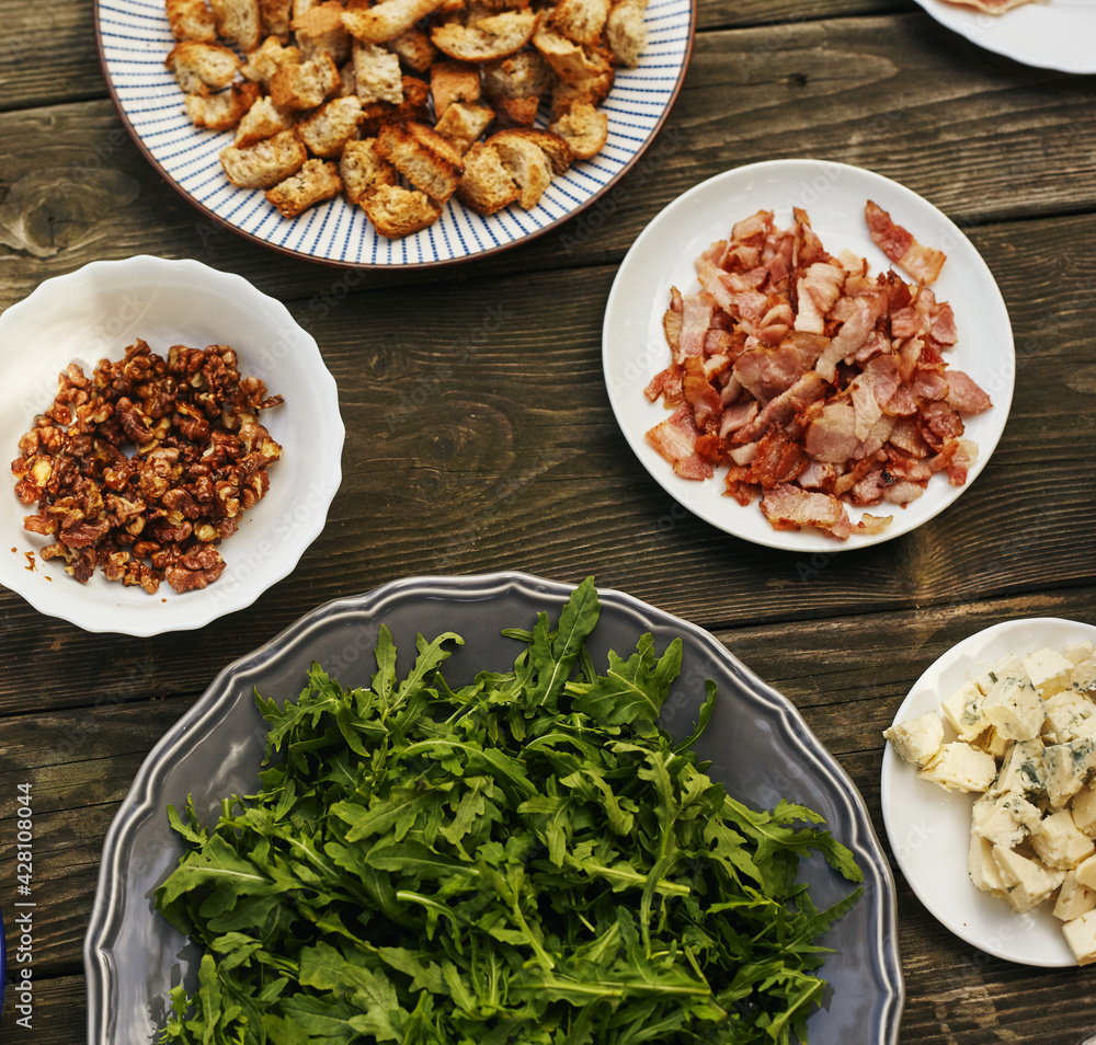 Ingredients for arugula salad, blue cheese, prosciutto, pear and caramelized nuts on an old table. Top view Ingredients for arugula salad, blue cheese, prosciutto, pear and caramelized nuts on an old table. Top view