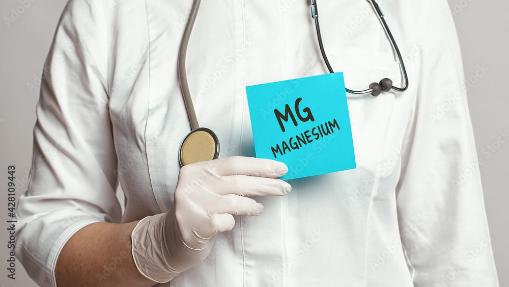 Cropped view of doctor in a white coat and sterile gloves holding a note with text - MAGNESIUM - obrazy, fototapety, plakaty 