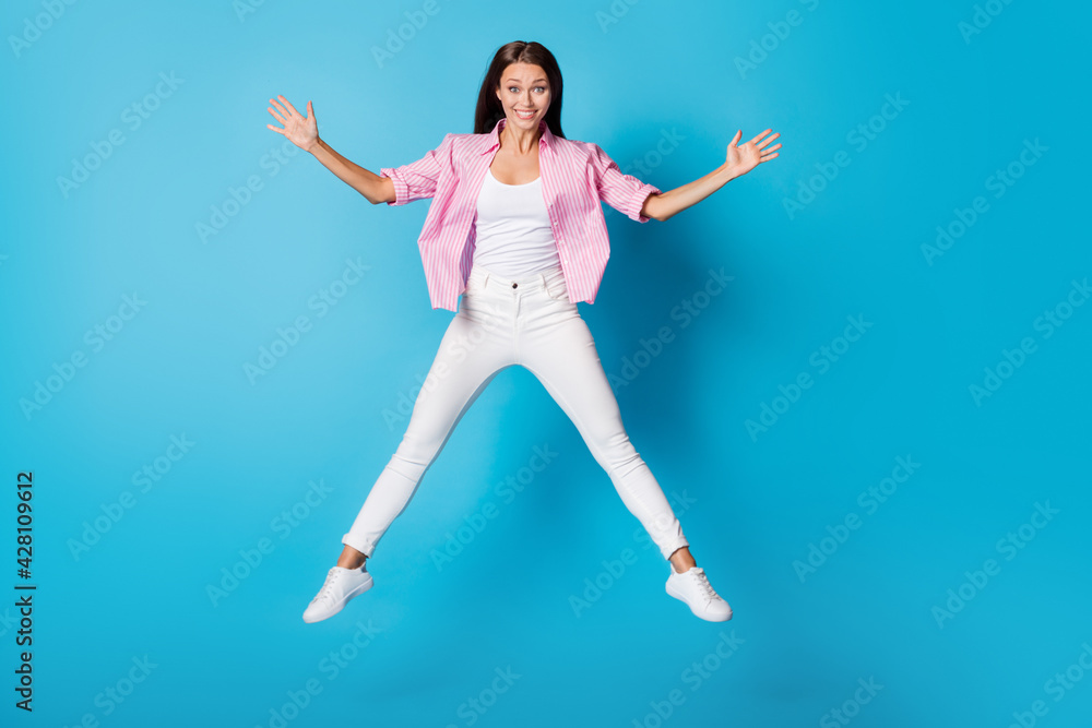 Photo of lady jump raise palms toothy smile wear pink striped shirt pants footwear isolated blue background Photo of lady jump raise palms toothy smile wear pink striped shirt pants footwear isolated blue background