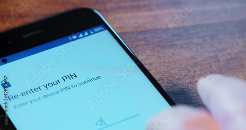 Man sets unlock pin-code in application of contemporary mobile phone with white screen on wooden table extreme close view