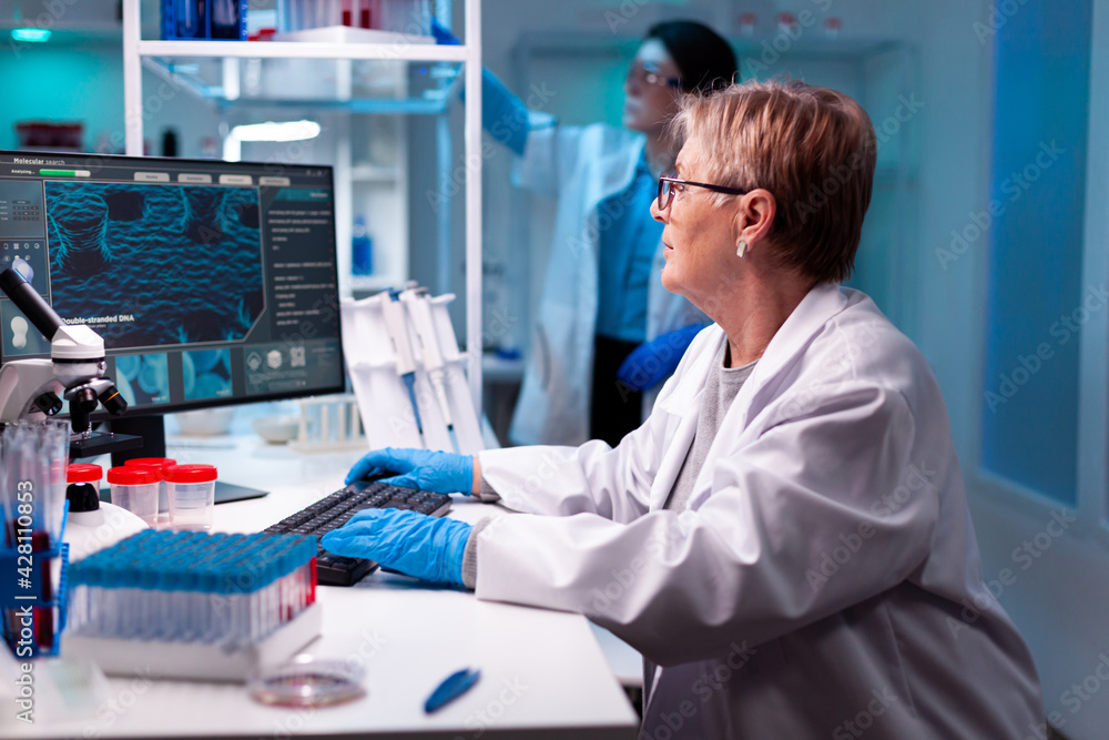 Senior scientist in chemical science laboratory study with team, test tubes, micropitette. Doctor examining vaccine evolution using high tech for scientific research, treatment development. Senior scientist in chemical science laboratory study with team, test tubes, micropitette. Doctor examining vaccine evolution using high tech for scientific research, treatment development.