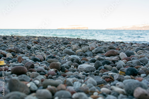 Black pebbles on a black sand beach in Santorini island, Greece. Sunny day, calm sea.