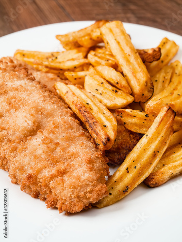 Traditional fish and chips dish on white plate. Common take away meal in English speaking nations. Cooked cod with peppered potato fries. Close up, vertical image
