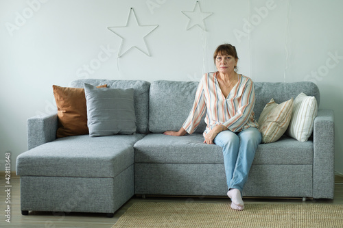 senior woman looking at camera, happy old lady posing at home indoor, positive single senior retired female sitting on sofa in modern living room.
