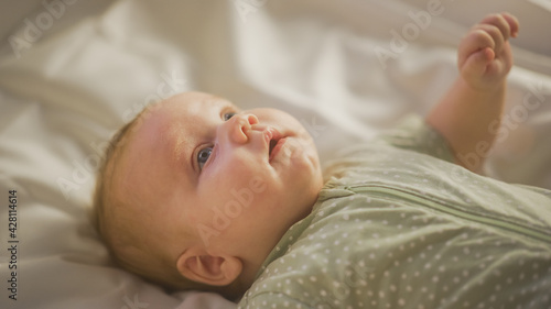 Authentic Close Up Shot of a Cute Newborn Baby Lying on the Back in Child Crib. Playful Portrait of a Caucasian Neonate Toddler at Cozy Home Space. Concept of Childhood, New Llife and Parenthood.