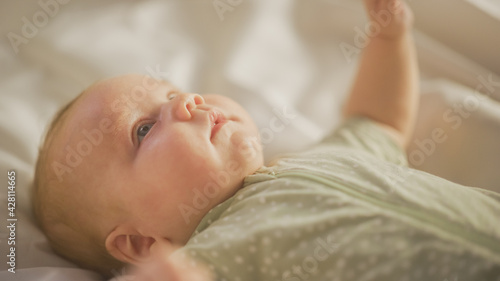 Authentic Close Up Shot of a Cute Newborn Baby Lying on the Back in Child Crib. Playful Portrait of a Caucasian Neonate Toddler at Cozy Home Space. Concept of Childhood, New Llife and Parenthood.