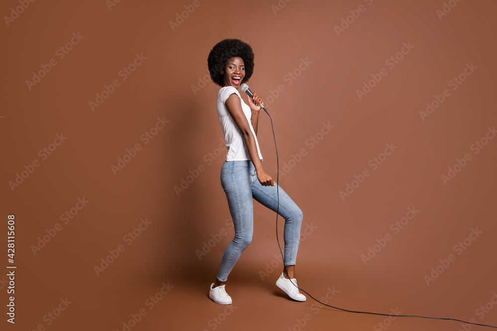 Full length body size photo of girl curious singing in microphone karaoke club entertaining isolated on brown color background Full length body size photo of girl curious singing in microphone karaoke club entertaining isolated on brown color background