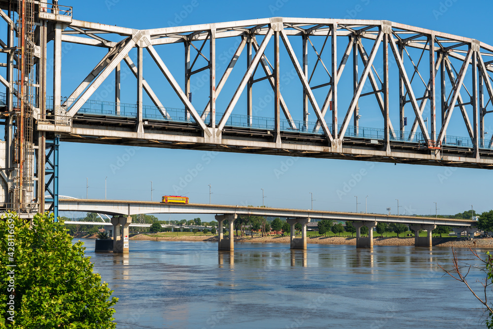 Junction Bridge over Arkansas River in Little Rock, Arkansas, USA. Historic railroad bridge, converted to a pedestrian bridge. In the distance, yellow streetcar crossing the river. Junction Bridge over Arkansas River in Little Rock, Arkansas, USA. Historic railroad bridge, converted to a pedestrian bridge. In the distance, yellow streetcar crossing the river.