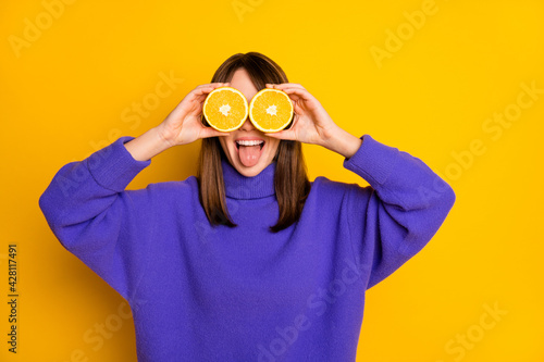 Portrait of attractive funny cheerful girl holding in hands orange slices closing yees having fun isolated over bright yellow color background photo