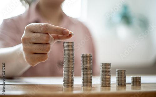 A woman is holding coins in five rows from low to high, she is accounting for income and expenses and dividing her savings. Concept of saving money and investing it to grow money.