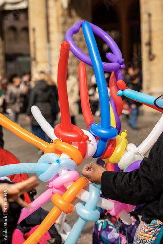Closeup of a balloon seller with multi colored balloons in the shape of a sword and heart during the Carnival in Bologna city, Emilia Romagna, Italy, Europe.