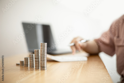 Stacked coins on a woman's desk, she was doing income and expenditure accounts to divide the money into savings and to buy funds to grow. Concept of saving money and investing.