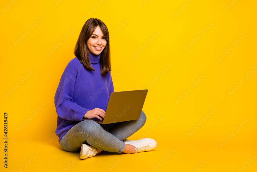 Full size photo of young smiling good mood girl sit on floor working in laptop isolated on yellow color background Full size photo of young smiling good mood girl sit on floor working in laptop isolated on yellow color background