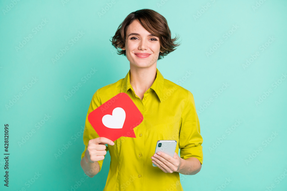 Photo portrait of girl keeping cellphone showing like icon isolated on vivid turquoise color background Photo portrait of girl keeping cellphone showing like icon isolated on vivid turquoise color background