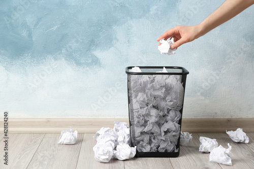 Woman throwing crumpled paper ball into basket near light blue wall, closeup. Space for text