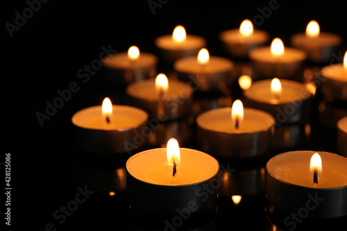 Many burning tea candles on black background, closeup