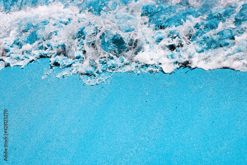 Deep water, stormy waves and sandy beach toned in blue. Beautiful coastline with copy space. Top view. Pop art concept. Summer Banner with copy space