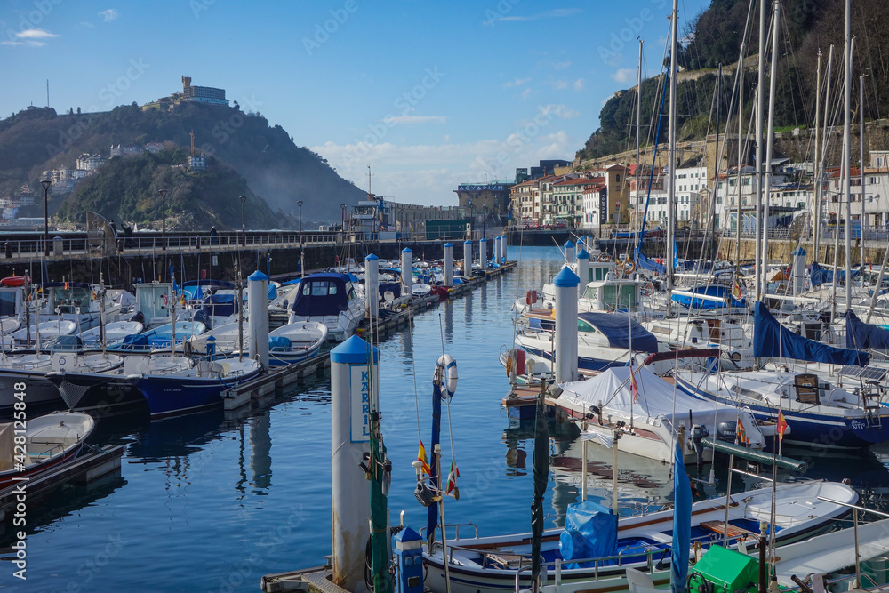 Obraz premium San Sebastian, Spain - April 2, 2021: Boats in the marina in La Concha Bay at the foot of Mt. Urgull