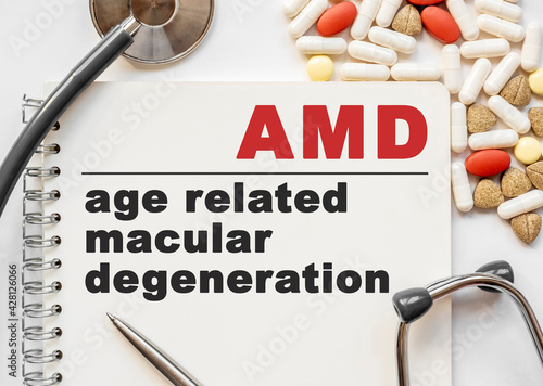 Page in notebook with AMD age related macular degeneration on white background with stethoscope and group of pill. Medical concept. Term and abbreviation