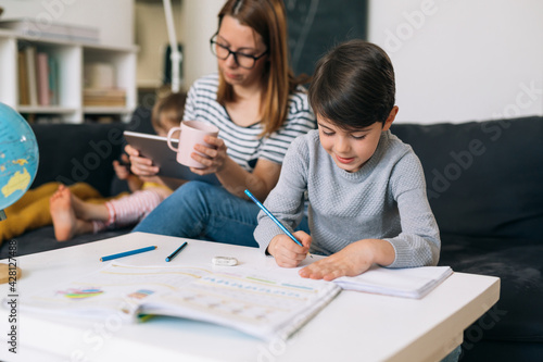 little boy does his homework at home. mother sitting beside him