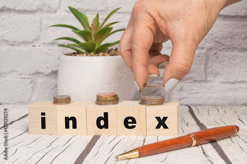 Index is a word written in wooden cubes. Office background with pen, coins, hand