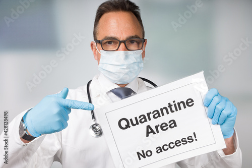 Doctor with medical face mask and medical gloves pointing to a quarantine sign in front of a restricted area