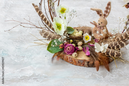 Easter composition with easter bunny, eggs, feathers and flowers on grey background, space for text