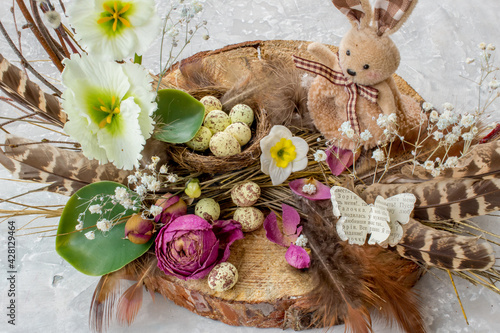 Easter composition with easter bunny, eggs, feathers and flowers on grey background