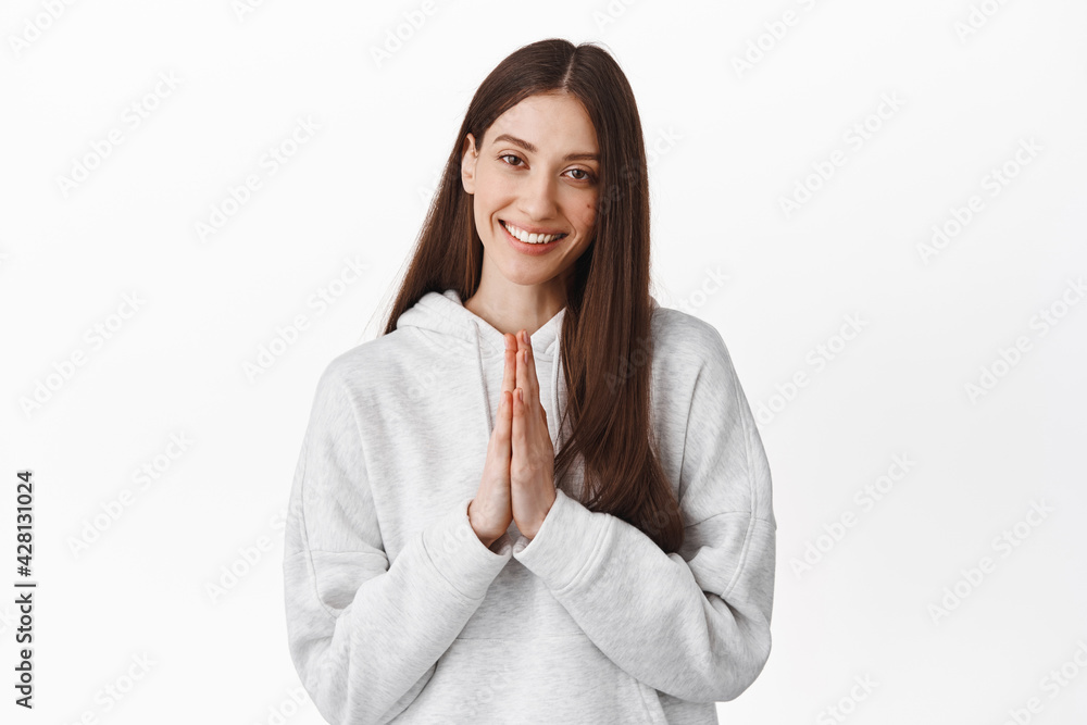 Thank you, namaste. Smiling young woman look caring and pleased, holding hands in beg pray gesture, being grateful, appreciate help, standing over white background Thank you, namaste. Smiling young woman look caring and pleased, holding hands in beg pray gesture, being grateful, appreciate help, standing over white background