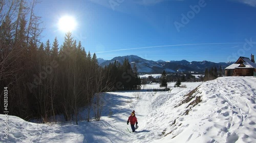 Time lapse of kid in red jacket sledding through the hill during winter sunny day with clear sky in Zakopane, Poland. Tatry mountains in the background.