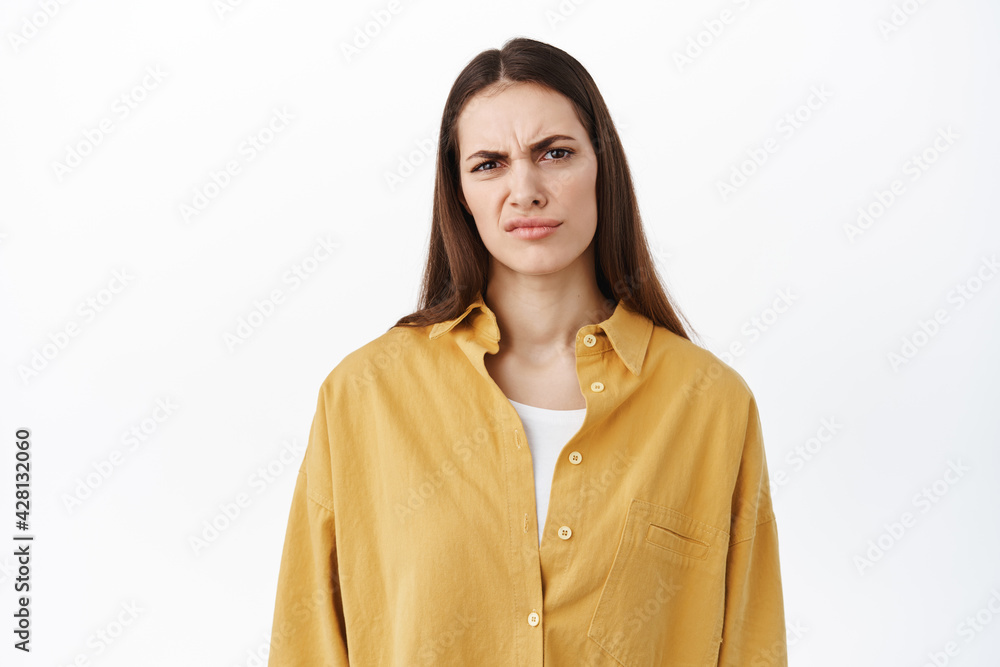 Woman grimacing and frowning as looking at something bad, cringe from awful content, stare disappointed and judgemental, judging express dislike, standing over white background Woman grimacing and frowning as looking at something bad, cringe from awful content, stare disappointed and judgemental, judging express dislike, standing over white background
