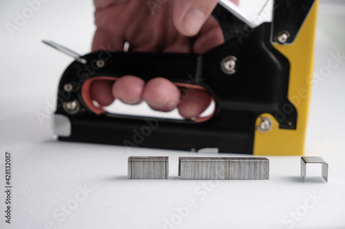Metal staples on a blurred background of a staple gun in a man's hand. White foam rubber background. 