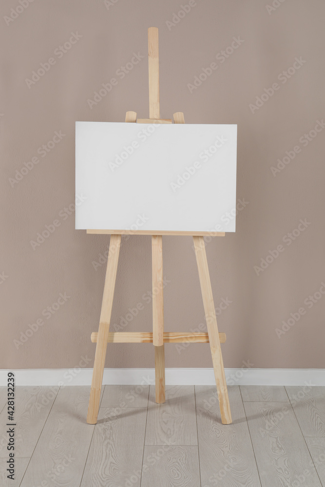 Wooden easel with blank canvas near beige wall Wooden easel with blank canvas near beige wall