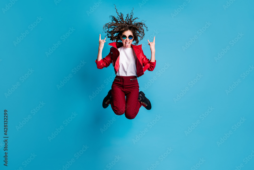 Full size portrait of carefree lady jump high show heavy metal symbol tongue out isolated on blue color background Full size portrait of carefree lady jump high show heavy metal symbol tongue out isolated on blue color background