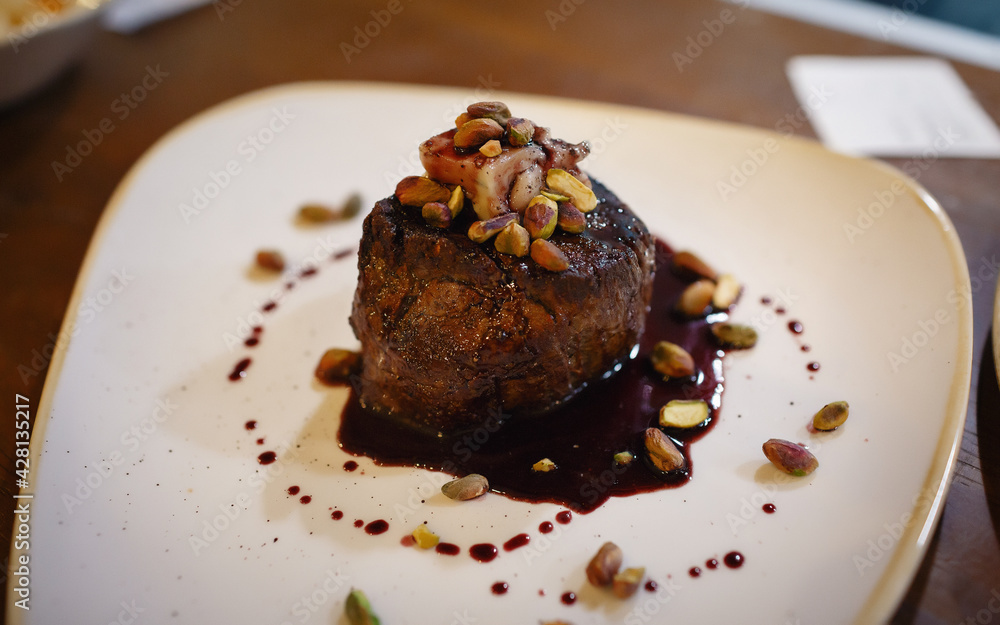 An oval slice of roasted beef sprinkled with pistachios and sprinkled with sauce. Well-done meat nicely served in a white plate restaurant. An oval slice of roasted beef sprinkled with pistachios and sprinkled with sauce. Well-done meat nicely served in a white plate restaurant.
