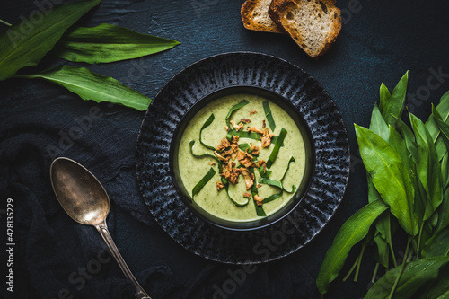 Wild garlic soup with wild garlic leaves and rosted onions on black background, top view photo