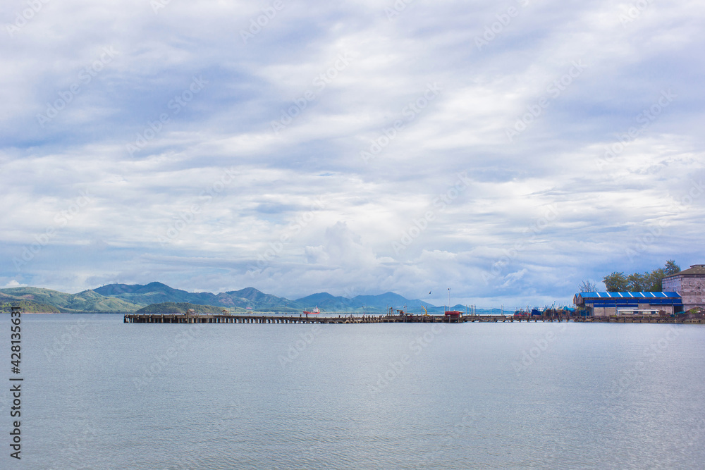The sea view and port with sky is full of clouds. There is mountain on background.